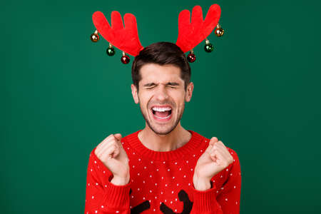 Photo portrait man in red knitted sweater with reindeer horns shouting crazy isolated green color backgroundの写真素材