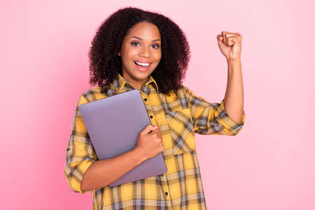Photo of cheerful lady hold netbook gadget raise fist rejoice wear checkered shirt isolated pink color backgroundの写真素材