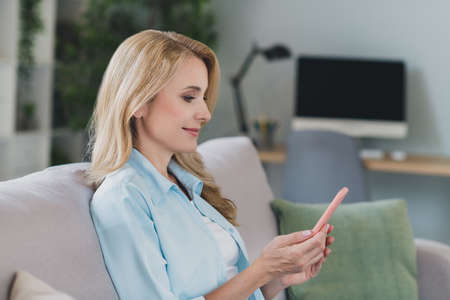 Photo of mature charming pretty lady hold telephone enjoy free time wear blue shirt home apartment indoorsの写真素材