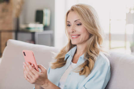 Photo portrait woman blonde hair smiling sitting on sofa using mobile phone social media