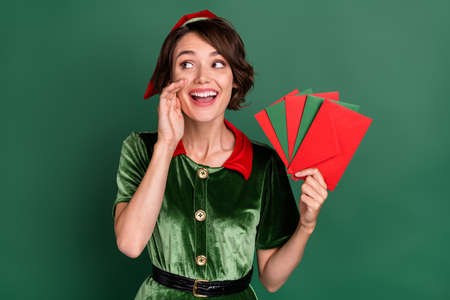 Photo of dreamy lady hold fan envelop look empty space tell secret wear elf costume hat isolated green color backgroundの写真素材
