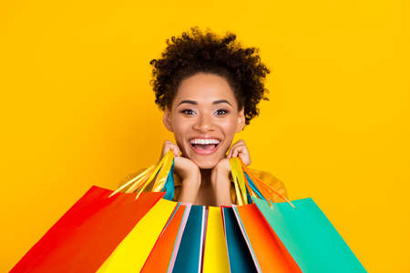 Photo of young cheerful black girl good mood shopaholic bag mall sale isolated over yellow color backgroundの写真素材