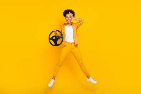 Full length body size photo woman jumping keeping steering wheel amazed isolated vivid yellow color backgroundの写真素材
