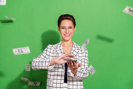 Photo of sweet adorable young woman dressed checkered clothes glasses throwing dollars smiling isolated green color backgroundの写真素材