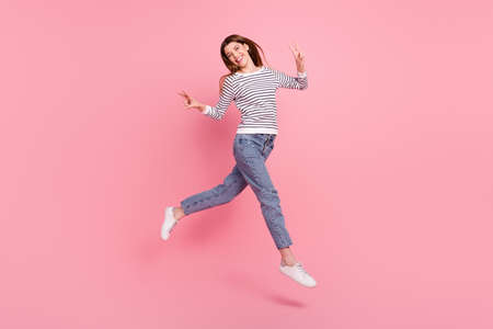 Full length body size view of attractive cheerful girl jumping showing v-sign going isolated over pink pastel color backgroundの写真素材