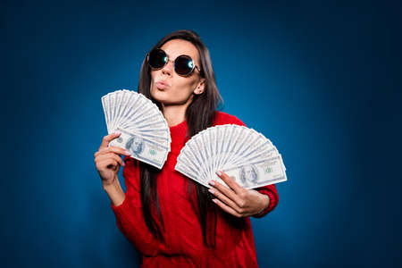 Photo of cool funny young lady wear knitted sweater dark glasses lips pouted holding usd fan isolated gradient blue color backgroundの写真素材