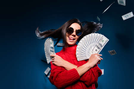 Photo of cool brown hair lady hold money tongue out wear spectacles red sweater isolated on blue color backgroundの写真素材