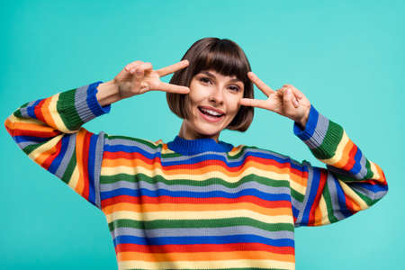 Photo portrait smiling girl in pullover showing v-sign gesture isolated vivid teal color backgroundの写真素材