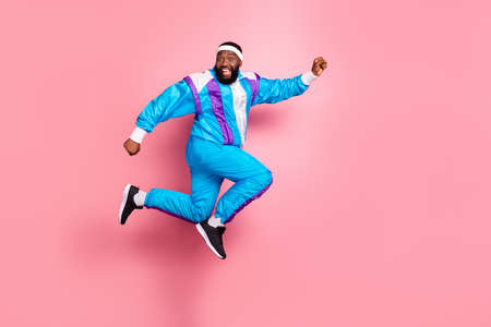 Photo of excited pretty dark skin guy dressed sport suit headband smiling jumping high running fast isolated pink color backgroundの写真素材
