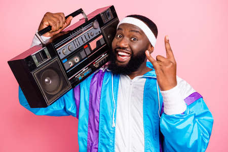 Photo of charming cool dark skin guy dressed sport suit headband smiling listening boom box showing rock sign isolated yellow color backgroundの写真素材