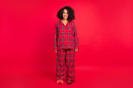 Full body photo of happy young afro american woman wear sleepwear holiday spirit smile isolated on red color backgroundの写真素材
