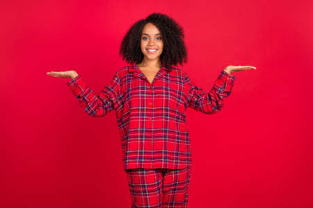 Photo of positive happy young afro american woman hold hands scales empty space object isolated on red color backgroundの写真素材