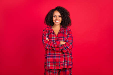 Photo of confident young afro american woman hold hands crossed smile pajama party isolated on red color backgroundの写真素材