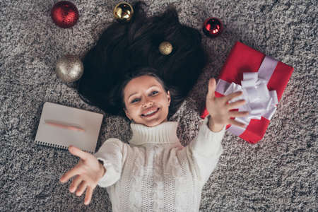Photo of pretty dreamy young woman dressed knitted sweater lying floor rising arms smiling indoors room home houseの写真素材