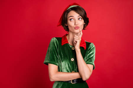 Photo of minded dreamy positive happy woman santa helper elf look empty space xmas isolated on red color backgroundの写真素材