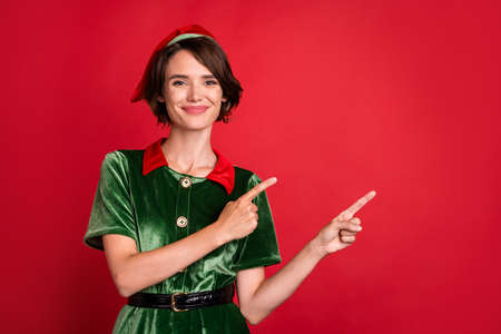Photo of young happy lady santa helper point fingers empty space christmas sale isolated on red color backgroundの写真素材