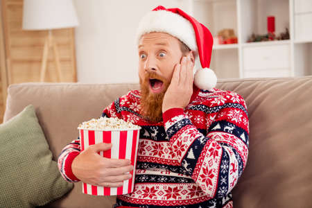 Photo of young man amazed shocked surprised omg wow reaction hold popcorn box watch movie thriller new year indoorsの写真素材