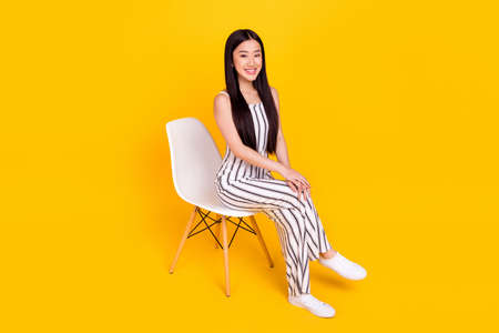 Full length body size photo young girl sitting on chair wearing casual overall smiling isolated vivid yellow color backgroundの写真素材