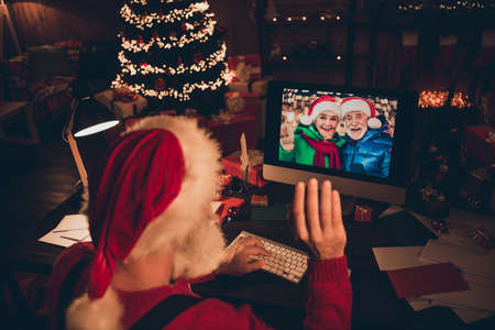 Photo of sweet pretty mature man dressed santa costume speaking modern gadget waving arm indoors home roomの写真素材
