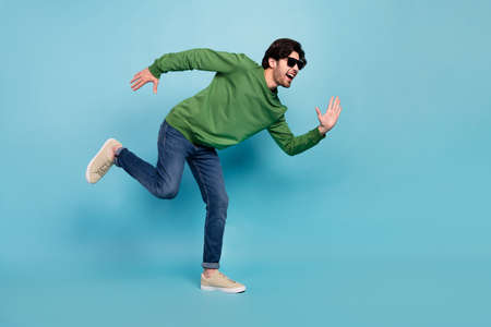 Full body photo of young good mood handsome guy in sunglass run fast speed isolated on blue color backgroundの写真素材