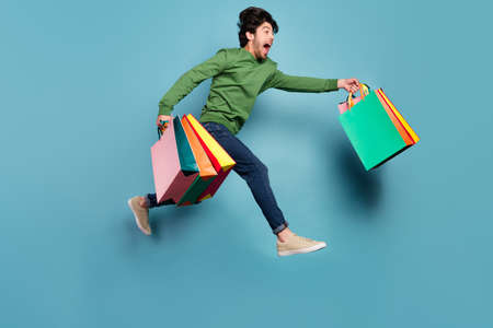 Full body profile side photo of crazy smiling guy running shopaholic black friday isolated on blue color background