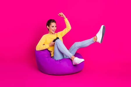 Photo of pretty lucky young woman dressed yellow pullover sitting bean holding playstation rising...