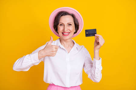 Photo of mature business woman happy positive smile thumb-up like advert choice credit card isolated over yellow color backgroundの写真素材