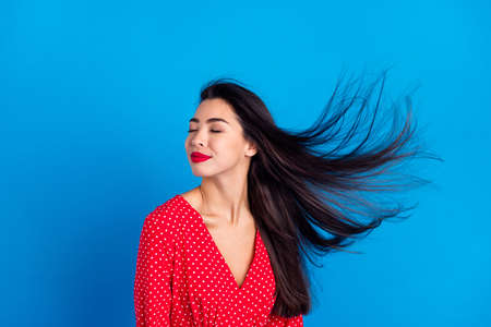 Photo portrait of smiling woman dreamy in red dress with flying hair isolated on vivid blue color backgroundの写真素材