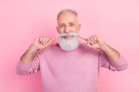 Photo of cheerful grey hair aged man point beard wear pink sweater isolated on pastel color backgroundの写真素材