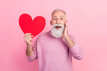 Photo of impressed grey hair mature man hold heart wear pink sweater isolated on pastel backgroundの写真素材