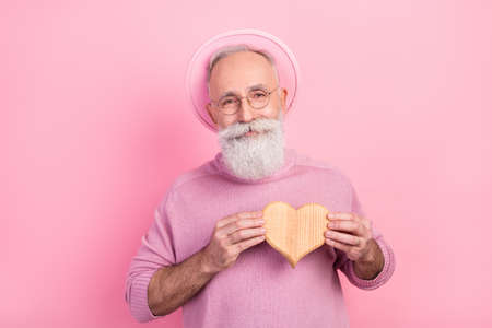 Photo of flirty grey hair senior man hold heart wear eyewear headwear sweater isolated on pink backgroundの写真素材