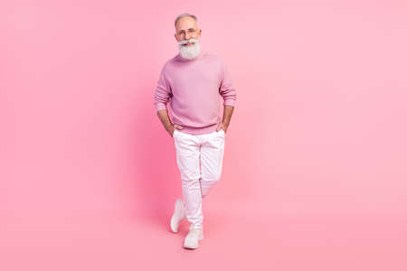 Photo of cute charming mature man dressed pullover glasses smiling walking arms pockets isolated pink color backgroundの写真素材