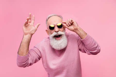Photo of funky cool mature man dressed pullover arm dark glasses smiling waving arm hello isolated pink color backgroundの写真素材