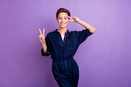 Photo of crazy millennial short hairdo lady show v-sign wear jeans overall isolated on violet color backgroundの写真素材