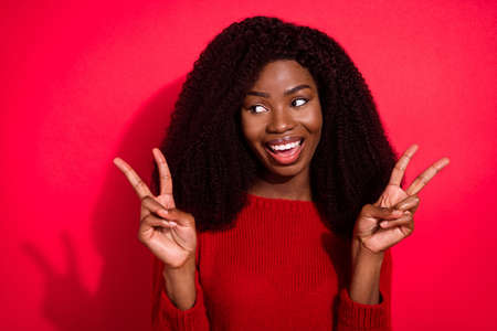 Photo of young black girl happy positive smile show v-sign hi hello symbol isolated over red color backgroundの写真素材