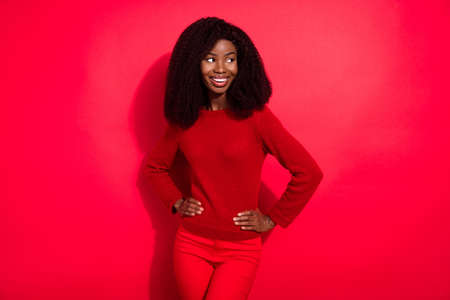 Photo of adorable shiny dark skin lady wear casual sweater smiling arms waist looking empty space isolated red color backgroundの写真素材