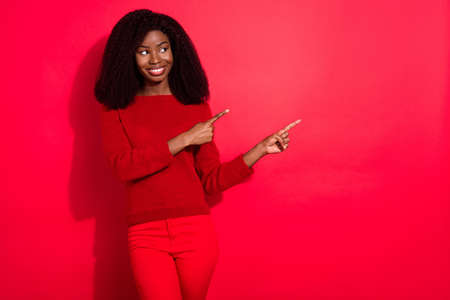 Photo of young black girl happy positive smile look indicate fingers empty space ad choice promo isolated over red color backgroundの写真素材