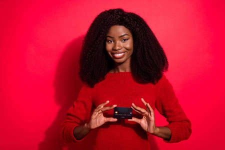 Portrait of attractive cheerful girl holding in hands bank card modern paypass method isolated over bright red color backgroundの写真素材