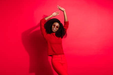 Photo of young cheerful african girl happy positive smile hands up wear sunglass isolated over red color backgroundの写真素材