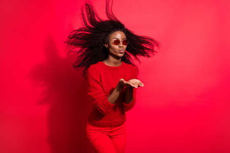 Photo of pretty adorable dark skin woman dressed casual pullover sending kiss arms empty space isolated red color backgroundの写真素材