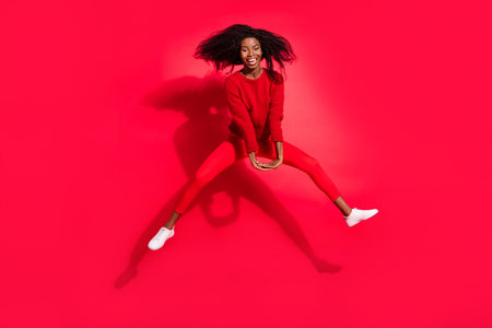 Full length photo of young black girl happy positive smile have fun jump up isolated over red color backgroundの写真素材
