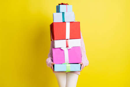 Lady holds many gifts cover against wear white pants isolated on vivid yellow color backgroundの写真素材