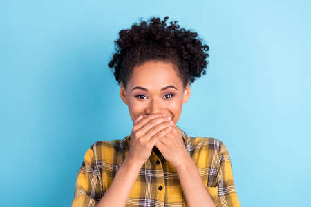 Photo portrait curly woman wearing checkered shirt covered mouth with hands keeping secret isolated pastel blue color backgroundの写真素材