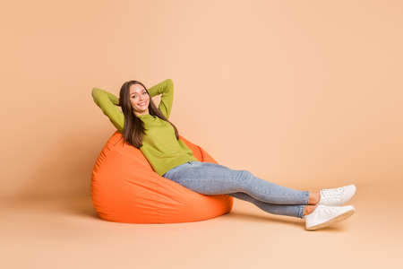 Full length body size view of nice pretty cheerful girl lying in orange bag chair resting isolated over beige pastel color backgroundの写真素材