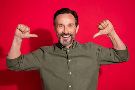 Photo of funny mature brunet man point himself wear khaki shirt isolated on red color backgroundの写真素材