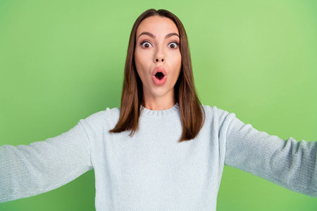 Photo of impressed young brunette lady do selfie wear blue jumper isolated on green color backgroundの写真素材