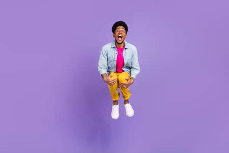 Photo of positive cheerful guy jump arms cuddle knees wear blue shirt pants shoes isolated purple color backgroundの写真素材