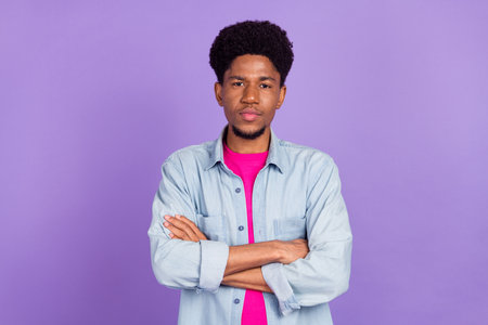 Photo of cute serious dark skin man wear denim shirt hands folded isolated purple color backgroundの写真素材