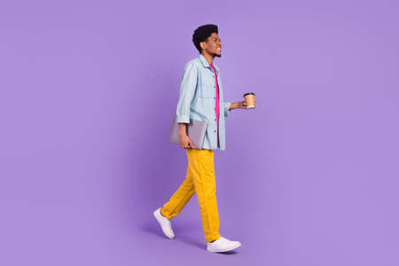 Photo of funky cute man wear denim walking drinking tea looking empty space holding gadget isolated purple color backgroundの写真素材