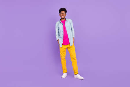 Photo of cute funny dark skin guy dressed jeans shirt arms pockets smiling isolated violet color backgroundの写真素材
